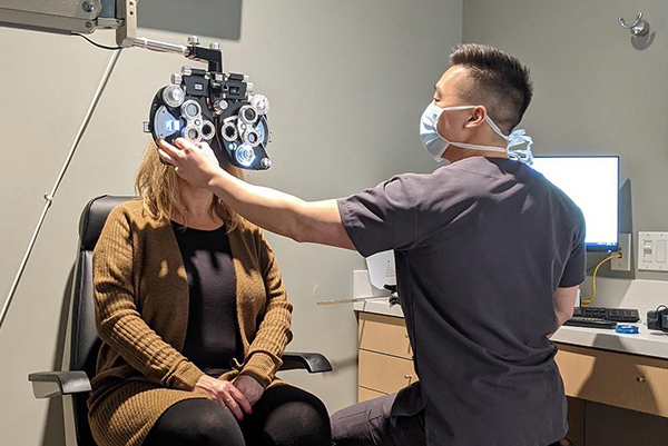 Optometrist checking patient’s eyes with phoropter in exam room - Dr. Kamachi